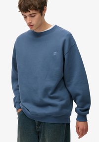 Blauwe katoenen sweatshirt met een geribbelde halslijn en manchetten. Heeft een klein geborduurd logo op de linkerborst en een relaxte pasvorm.