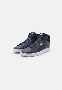 Tumesinised mid-top sneakers tumepruuni nahaga mustade aktsentidega, valge kummitald ja pehmendusega kaelus. Omab nööre ja Puma logo keeles.