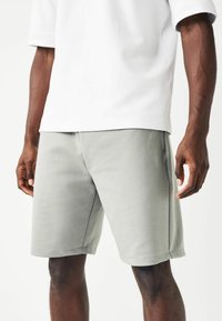 Shorts gris clair, fabriqués à partir d'un tissu doux, avec une taille élastique et des poches latérales. Coupés au-dessus du genou avec des détails de couture subtils.