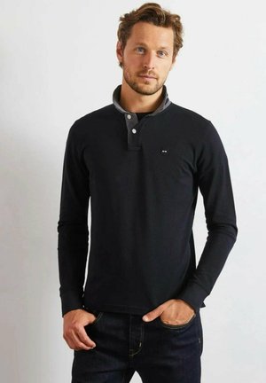 Polo noir à manches longues avec col gris et patte de boutonnage à trois boutons. Présente un petit logo sur la poitrine et des poignets côtelés. Associé à un jean foncé.