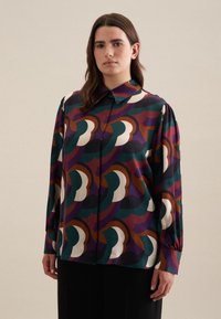 Blusa a maniche lunghe con un motivo astratto multicolore nei toni di verde, viola, marrone e crema. Realizzata in un tessuto morbido e leggero.