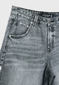 Jeans en denim gris avec une taille haute, des détails déchirés, deux poches avant, des garnitures en argent et une étiquette à la taille.