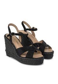 Sandales à talons compensés noires avec orteils ouverts et détails de lanières entrecroisées, présentant des accents en clous et une plateforme tissée texturée. Bride de cheville réglable.