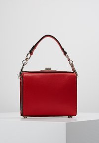 Sac à main en cuir rouge de forme carrée, avec une poignée courte, des ferrures argentées et une finition texturée. Dispose d'une fermeture à boucle sur le dessus.