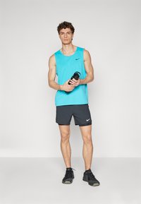 Turquoise sleeveless athletic top, black shorts, and black sneakers. Holding a black water bottle. Simple design with Nike branding.