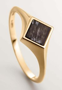 Anillo de oro con una banda lisa y un engaste cuadrado de piedra negra. La piedra tiene una superficie texturada con reflejos de luz.