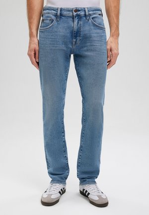 Light blue denim jeans with a straight fit, five pockets, and subtle faded detailing. Paired with white and gray athletic shoes.