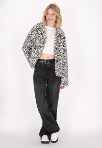 Giacca in pile con stampa leopardata nera e grigia, design con colletto, indossata sopra una maglietta bianca cropped e abbinata a jeans neri a vita alta.