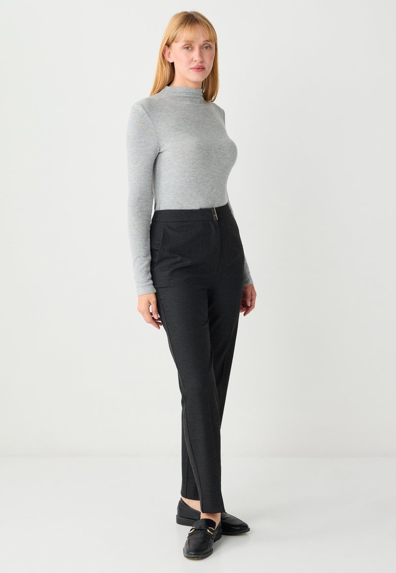Haut à manches longues gris associé à un pantalon noir ajusté. Le pantalon comporte une braguette zippée, des poches latérales et une coupe slim. Des mocassins noirs complètent la tenue.