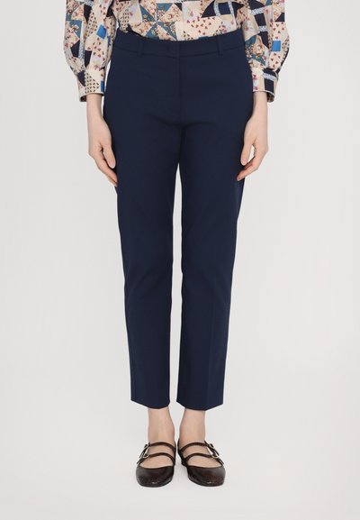Pantalons bleu marine ajustés avec une coupe slim, ourlet à revers et poches latérales, associés à des ballerines brunes à plusieurs brides.