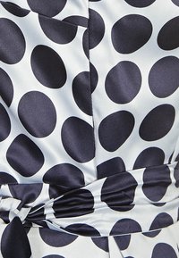 Tissu satin présentant un motif à pois bleu marine sur un fond clair ; inclut un détail de taille nouée et une texture lisse.