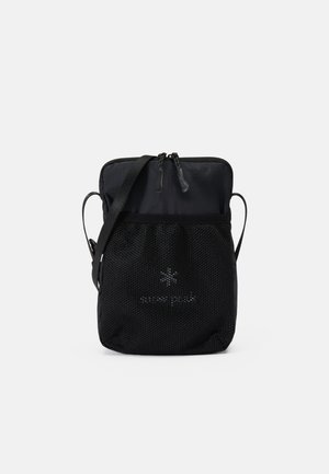 Borsa nera compatta con chiusura a zip, tasca frontale in rete, tracolla regolabile e dettaglio del logo. Realizzata in materiale resistente con un design minimalista.
