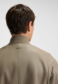 Beige läderjacka med ribbad krage, med en enkel design och en liten "BOSS"-logotyp på baksidan, slät textur.