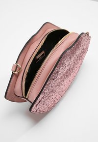 Vaaleanpunainen keinonahkainen laukku, jossa on kuvioitu kimalteleva etuosa, avoin vetoketju ja sileä sisävuori. Ominaisuuksiin kuuluu pyöreä muoto ja mustat yksityiskohdat.