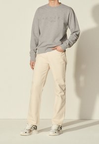 Sudadera gris con las palabras "sandro" y "PARÍS" en relieve, combinada con pantalones rectos de color beige claro y zapatillas blancas.