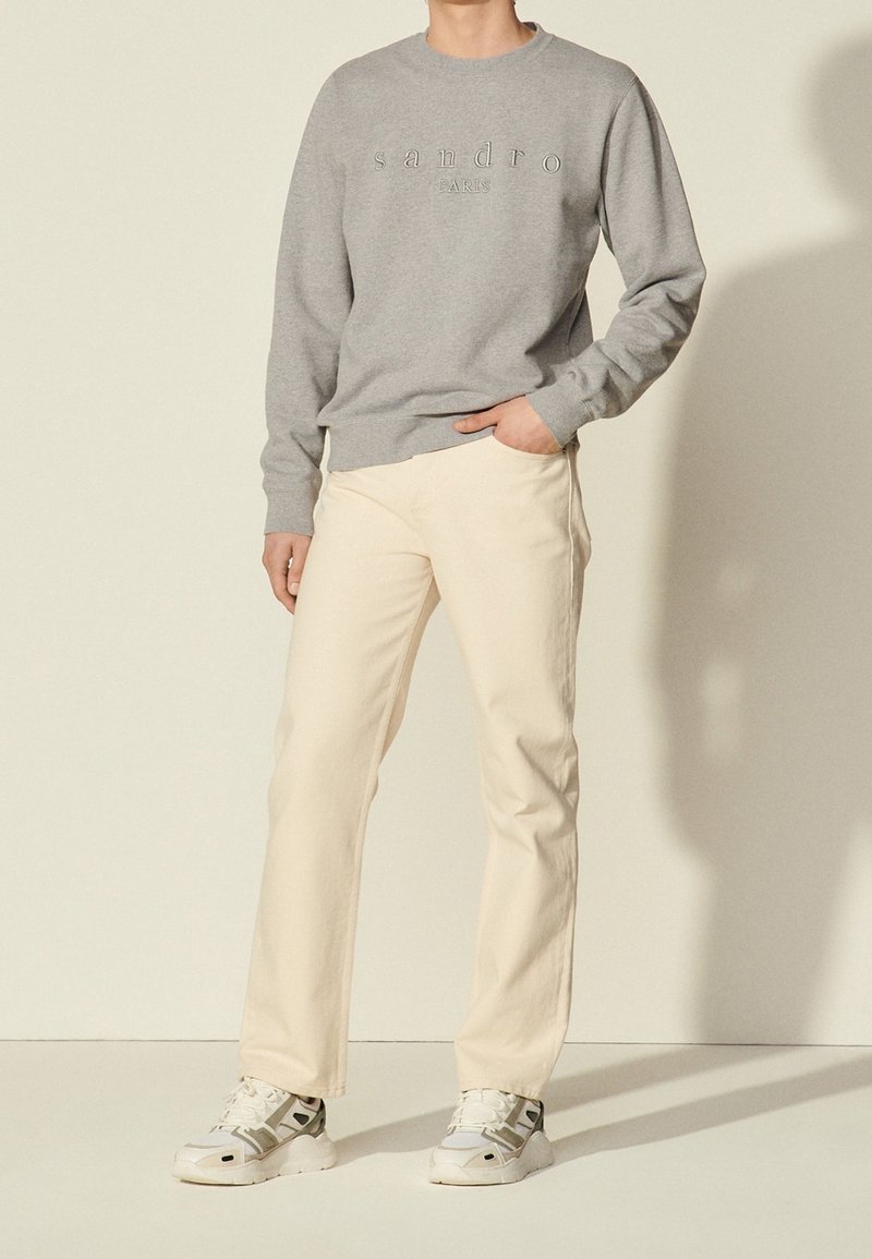 Sudadera gris con las palabras "sandro" y "PARÍS" en relieve, combinada con pantalones rectos de color beige claro y zapatillas blancas.