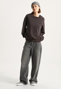 Dark gray sweatshirt with crew neck and ribbed cuffs, paired with loose-fitting gray jeans. Footwear features black and white checkerboard pattern.