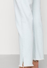 Ljusblå denimjeans med rak passform, med fransade fållar och slitsar för extra detalj. Tygets struktur är mjuk och något använd.