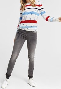 Light blue striped long-sleeve shirt with red and navy stripes and anchor patterns, paired with gray fitted jeans and white sneakers.
