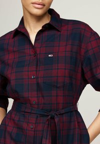 Rød og marineblå ternet skjorte med lange ærmer, knaplukning foran, brystlomme og en bundet taljebælte. Lavet af blødt, tekstureret stof.