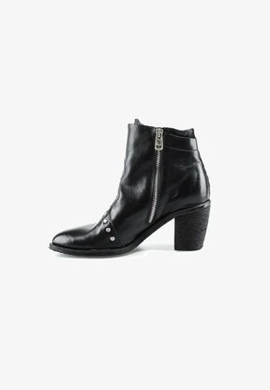Bottine en cuir noir avec talon épais, fermeture éclair latérale et clous argentés décoratifs près de la pointe sur fond blanc.