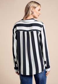 Schwarz-weiße gestreifte Langarmbluse mit plissiertem Rücken, Kragen und geknöpften Manschetten. Leichter Stoff auf neutralem Hintergrund.