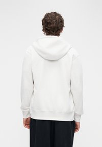 Λευκό βαμβακερό φούτερ με κουκούλα, εμπρός τσέπη τύπου καγκουρό, ριμπ μανσέτες, απαλή υφή και άνετη γραμμή· προβολή από πίσω.