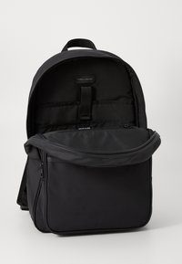 Black fabric backpack with a curved top, zippers, adjustable straps, and front pocket. Interior features organizational compartments.