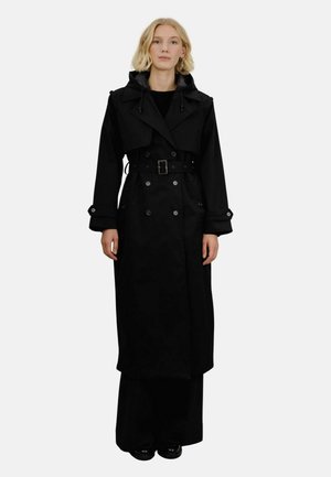 Lang svart trenchcoat med dobbeltradede knapper, belte og hette. Laget av glatt stoff med matte overflate.