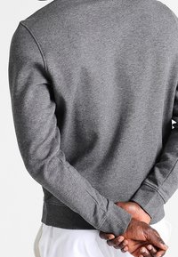 Grå tröja med lång ärm, ribbad mudd och rund halsringning. Mjuk textur med en enkel design utan logotyper eller mönster.