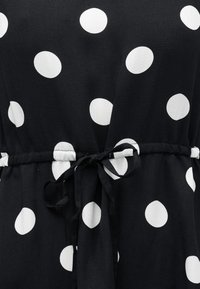 Μαύρο ύφασμα με μεγάλα λευκά πουά, με κορδόνι στη μέση που δένει.