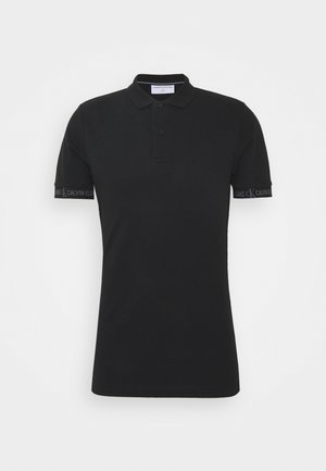 Czarna koszulka polo z klasycznym kołnierzykiem, krótkimi rękawami, zapięciem na dwa guziki i wyraźnie widocznym logo Calvin Klein na mankiecie rękawa.