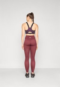 Bordeaux sportbeha en leggings van rekbaar materiaal. De beha heeft verstelbare banden en een uitsparing aan de achterkant. De leggings hebben een hoge taille en mesh-accenten.