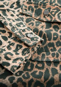 Grøn og beige leopardprintstof med en blød tekstur, der viser et nærbillede af sydde kanter og metalhardwareknapper.