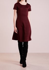 Vestido corto burdeos de mangas cortas con un patrón texturizado, cuerpo ajustado y falda acampanada, combinado con botas de ante negras hasta la rodilla.