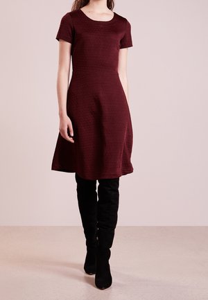 Robe bordeaux à manches courtes avec un motif texturé, corsage ajusté et jupe évasée, accompagnée de bottes hautes en suède noir.