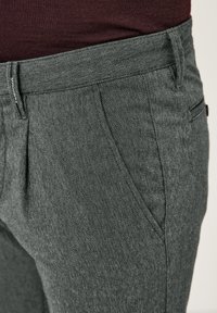 Graue, maßgeschneiderte Hose mit einem dezenten Fischgrätenmuster, ausgestattet mit Vordertaschen und einem sauberen Abschluss in der Taille. Weicher, strukturierter Stoff.