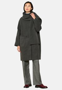 Cappotto di lana grigio con un ampio colletto, due tasche frontali e bottoni doppi. Abbinato a pantaloni a gamba larga argentati e scarpe bordeaux.