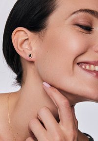 Złote kolczyki w kształcie kolców z czarnym owalnym kamieniem, osadzone w teksturowanej okrągłej ramie. Gładkie wykończenie z subtelnym blaskiem i minimalistycznym designem.