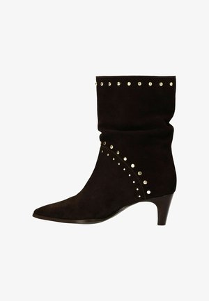 Bottine noire en daim avec un petit talon, bout pointu et clous en argent décoratifs le long des coutures supérieure et latérale.