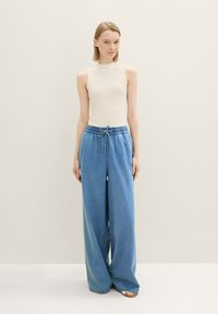 Top bianco a costine senza maniche abbinato a pantaloni in denim azzurro chiaro a gamba larga con vita elastica e cordoncino.