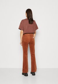 Camiseta corta marrón con mangas cortas combinada con pantalones de pana acampanados de color óxido que cuentan con bolsillos traseros y una etiqueta de marca en el lado derecho.