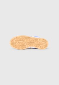 Rubber sneaker sole with a herringbone pattern, featuring a beige color and light blue upper with white accents. Flat, textured surface.