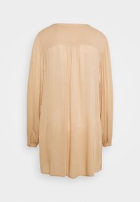 Chemise beige à manches longues avec un col rond, texture lisse, dos plissé et poignets boutonnés. Design simple, tissu léger.