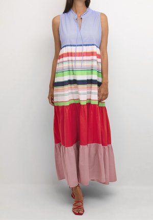 Robe maxi sans manches avec col à volants bleu, rayures horizontales multicolores, jupe à volants rouge et rose, portée avec des sandales rouges à brides.