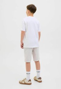 Vit t-shirt med kort ärm kombinerad med ljusgrå shorts. Beiga sneakers med bruna detaljer, vita strumpor med svart text. Enkel design.