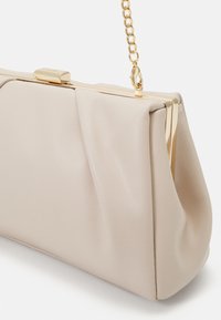 Sac pochette en cuir beige avec cadre métallique doré et bandoulière chaîne, doté d'une fermeture à fermoir rectangulaire sur le dessus.