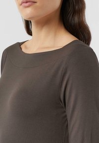 Brązowa bluzka z długim rękawem, z szerokim, zaokrąglonym dekoltem i gładkiego, elastycznego materiału. Skupienie na szczegółach ramion i dekoltu.