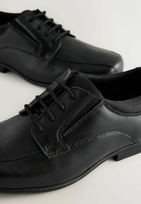 Chaussures habillées en cuir noir avec une finition lisse, dotées d'un design à lacets, de coutures contrastantes et d'une semelle en caoutchouc à profil bas.