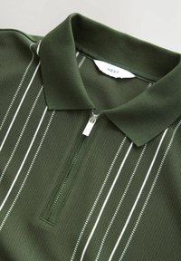 Zelené polotriko s krátkým zipem, vyrobené z texturované látky s bílými svislými pruhy, žebrovaným límcem a štítkem "NEXT".